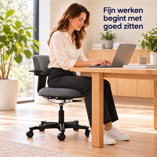 Vrouw met bruin haar in crèmekleurige blouse en zwarte broek werkt op laptop aan houten tafel.