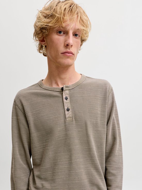 Model draagt een olijfgroen Henley-shirt met lange mouwen en knoopsluiting.
