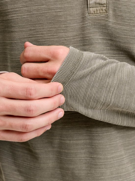 Detailopname van de wafelstructuur op de mouw van een olijfgroen Henley-shirt.