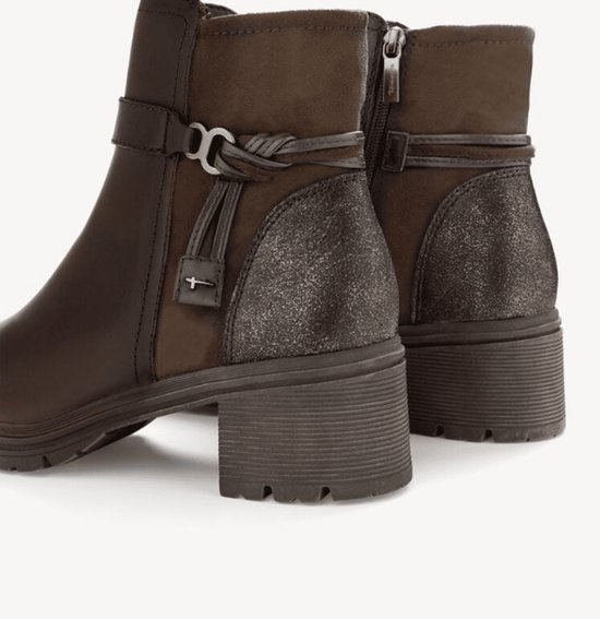 Detailopname van bruine Tamaris enkellaarsjes met gevlochten riempjes, metalen accenten en een glinsterende hiel.
