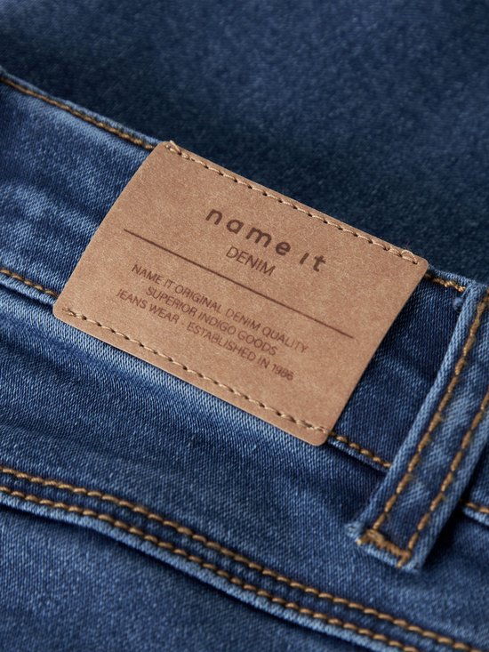 Close-up van een bruin leren label op een blauwe spijkerbroek met de tekst 'NAME IT DENIM'.