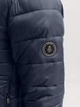 Detail van de mouw met een rond zwart merklabel met de tekst JACK & JONES SINCE 1990 CRAFTED IN BLUE.