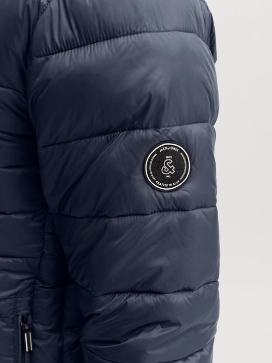 Detail van de mouw met een rond zwart merklabel met de tekst JACK & JONES SINCE 1990 CRAFTED IN BLUE.