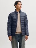 Model in een donkerblauw pufferjack met rits, gedragen over een beige gebreide trui en een jeans.