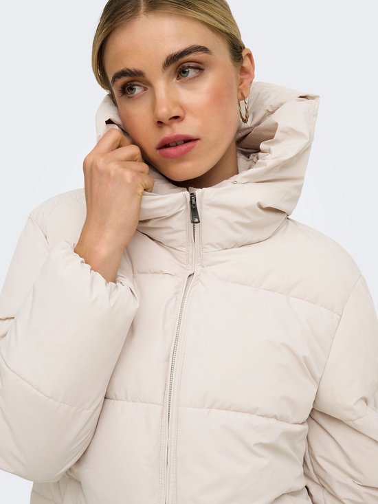 Close-up van het model in een beige pufferjas, waarbij de kraag wordt vastgehouden.