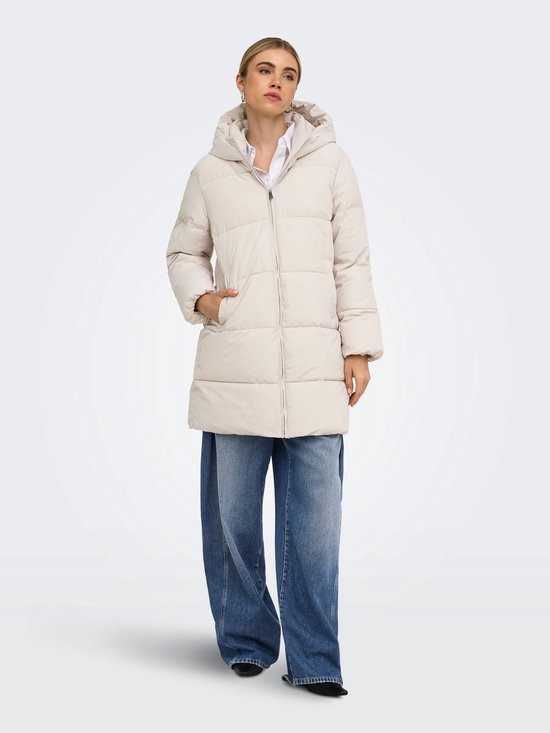 Model in een beige pufferjas met capuchon, gecombineerd met een wijde blauwe jeans.