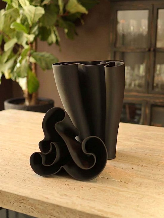 Zwarte 3D-geprinte vaas met golvend patroon, met los ornament ernaast.