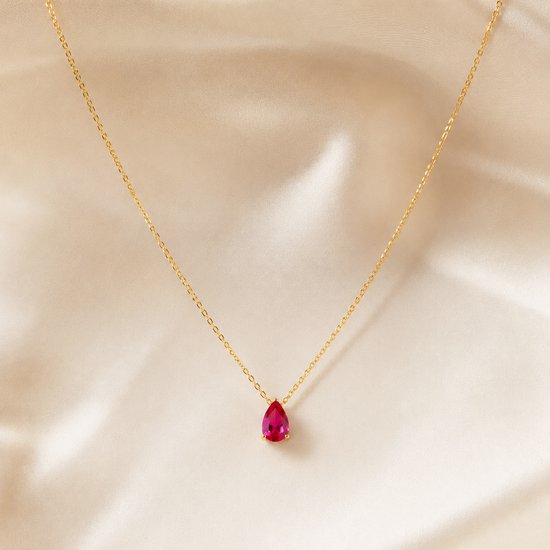 Gouden ketting met een rode robijnkleurige druppelvormige edelsteen op een crèmekleurige satijnen achtergrond.