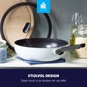 Blauw-grijze BK Enjoy wokpan met zwarte greep en deksel, op een aanrecht met keukenbenodigdheden en ingrediënten. Stijlvol design.