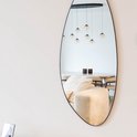 Organische wandspiegel met zwart frame, waarin een modern interieur met bank en hanglampen weerspiegeld wordt.