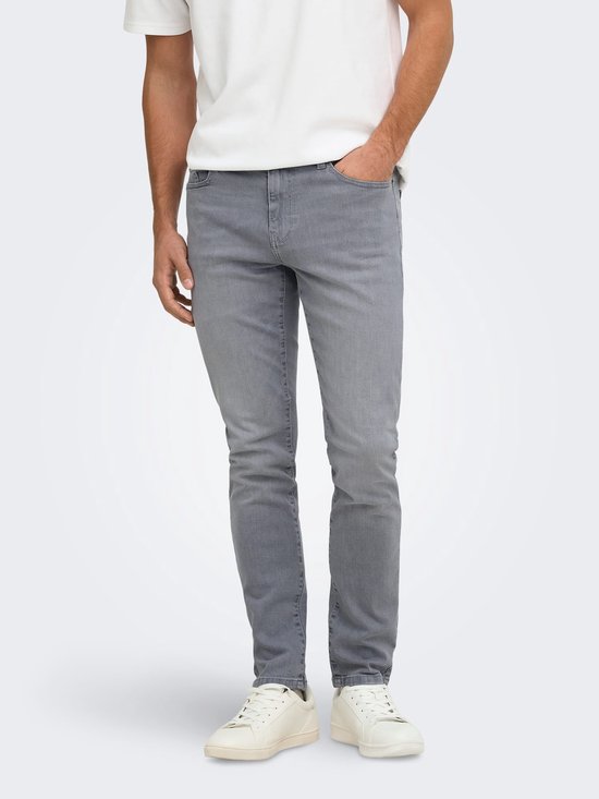 Model draagt een witte t-shirt, grijze slim fit jeans en witte sneakers.