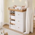 Vrouw die een baby verschoont op een wit-houten commode met drie lades en zijplanken in een kinderkamer.