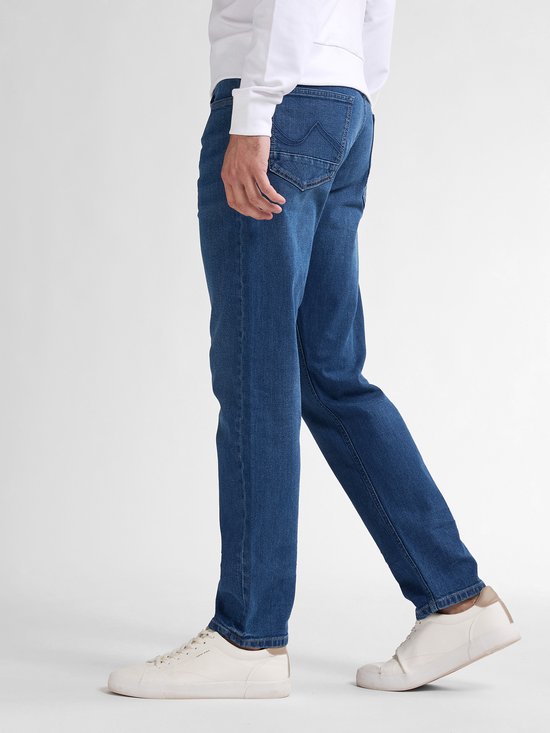 Model in een blauwe vintage wash jeans met tapered fit. De jeans heeft een 5-pocket ontwerp en is gemaakt van 98% katoen.