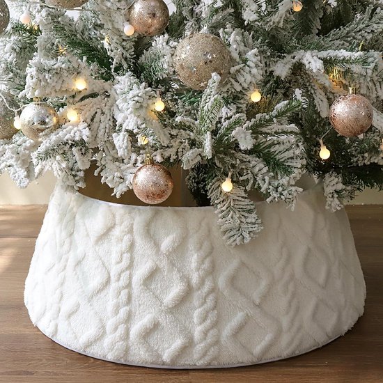 Crèmewitte boomkraag met pluche kabelpatroon onder een besneeuwde kerstboom met goudkleurige ornamenten.