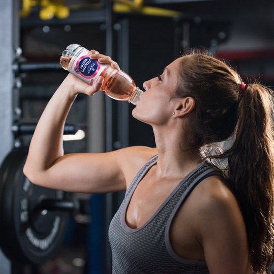 Sportieve vrouw drinkt Sourcy Vitamin Water Framboos Granaatappel in de sportschool.