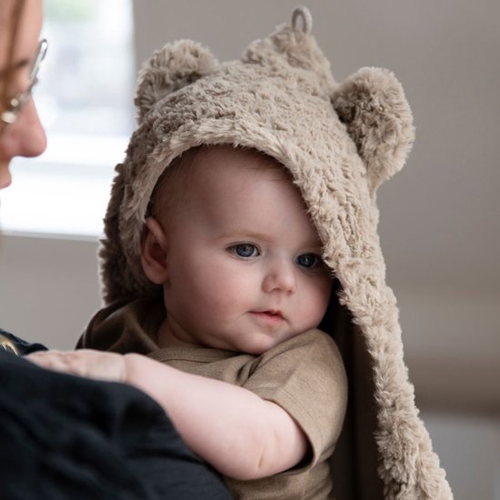 Un bébé aux yeux bleus dans une couverture enveloppante marron avec des oreilles d'ours.