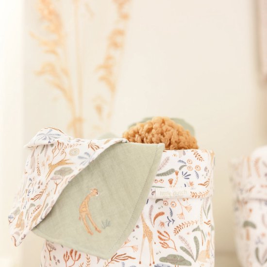 Opbergmand met safariprint: giraffen, bomen en bloemen in groen en oranje tinten. Een groene doek met girafprint steekt uit de mand.