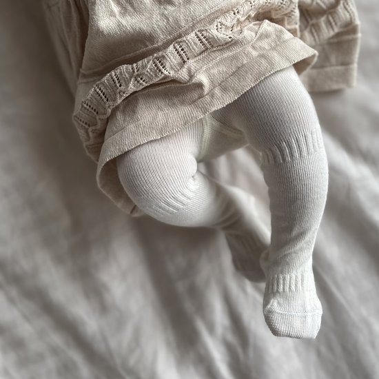 Babybeentjes in witte maillot met ribbelpatroon en gebreide details aan de jurk.