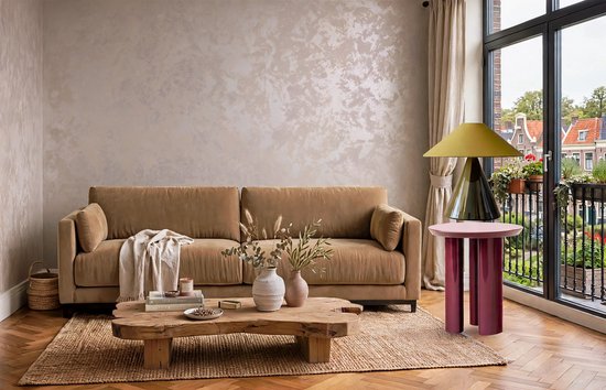 Een taupe bank met een beige textuurmuur en een houten salontafel met decoratie.