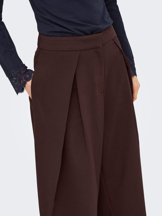 Close-up van bruine wijde broek met plooien en donkerblauw shirt met kanten mouwboorden.