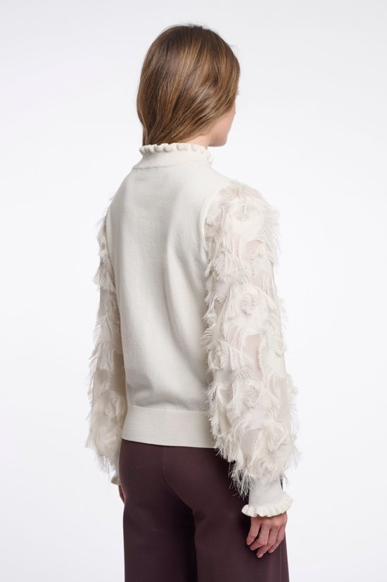 Achteraanzicht van een beige trui met een kraag met ruches en mouwen afgewerkt met decoratieve franjes.