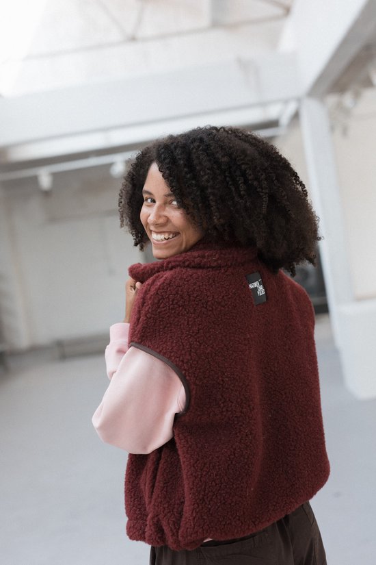 Model kijkt om in een bordeauxrode wollen bodywarmer met het 'Natural Wear Project' label.