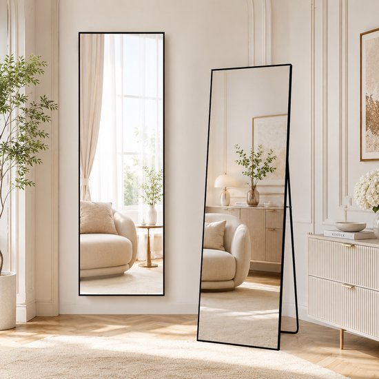 Slanke, staande en wandspiegel met zwart frame, in een lichte woonkamer.