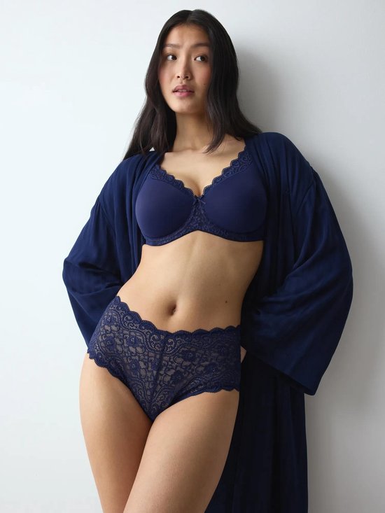 Model in een donkerblauwe beha, slip met kanten bies en bijpassende kamerjas.