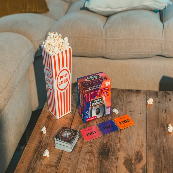 Doos met het spel Hitster Movies & TV Soundtracks, popcorn en vier kaarten met jaartallen: 1981, 1984, 2000.