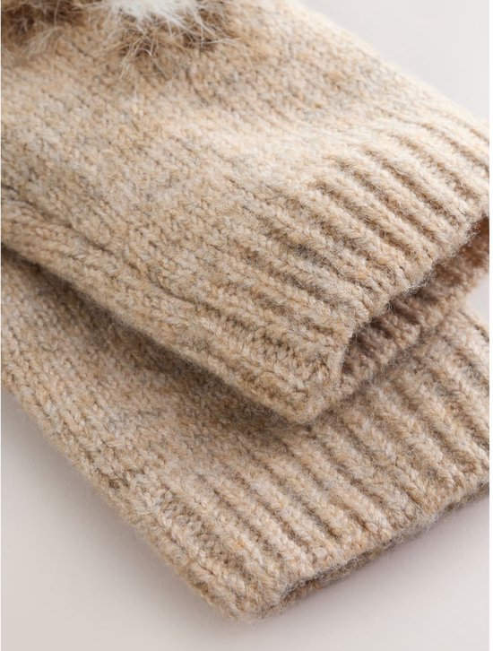Close-up van de geribbelde manchetten van een beige gebreide trui met witte en bruine pluizige applicaties.