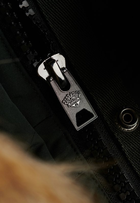 Close-up van de glanzende, zwarte rits van een donkergroene jas met Superdry-logo.