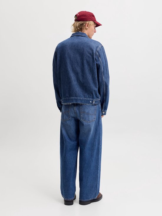 Man met korte blonde haren, donkerrode pet, jeansjack en wijde jeans.