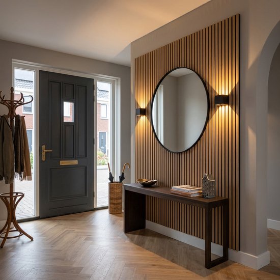 Entrée avec porte gris foncé, porte-manteaux et une console avec un miroir rond et deux appliques murales noires sur un lambris en bois.