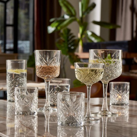 Diverse kristallen glazen op marmeren tafel, waaronder wijnglazen gevuld met witte wijn en waterglazen met munt.