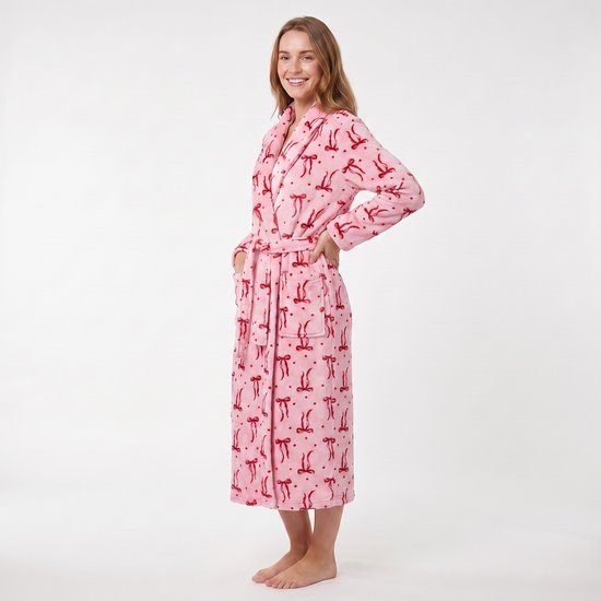 Vrouw staand in een roze badjas met rode strikjesprint, sjaalkraag en ceintuur.