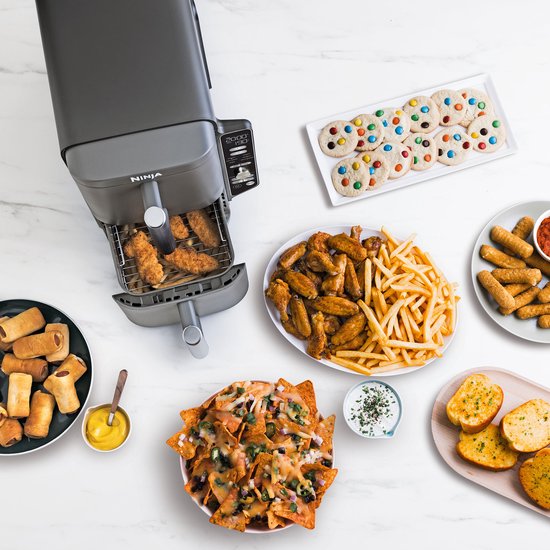 Zwarte Ninja heteluchtfriteuse, omringd door diverse snacks zoals kipnuggets, wings, nacho's en koekjes.