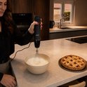 Vrouw gebruikt garde van zwarte staafmixer om eiwit op te kloppen, naast appeltaart.