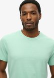 Gros plan d'un homme portant un t-shirt Superdry vert menthe.