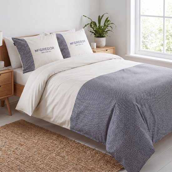 Un lit double avec une housse de couette beige et un motif à blocs bleu en bas. Deux oreillers avec "Mc GREGOR NEW YORK 1921" imprimé.