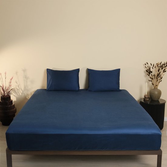 Donkerblauw katoensatijnen hoeslaken met twee bijpassende kussenslopen op een bed.
