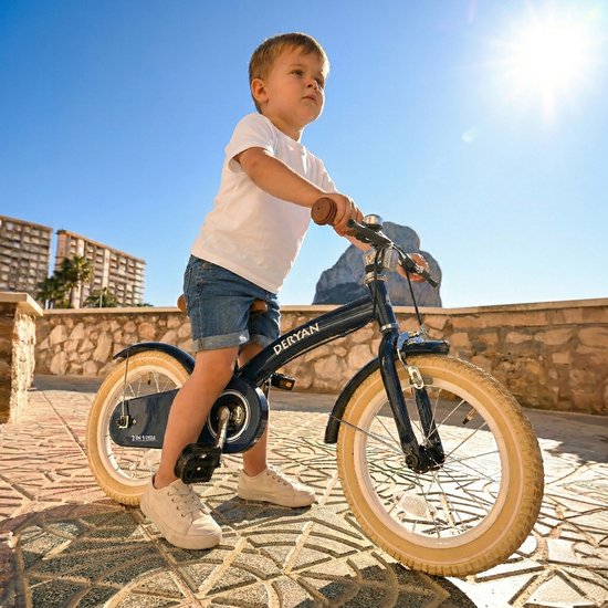 Petit garçon sur un vélo enfant Deryan bleu foncé avec pneus beiges et poignées marron.