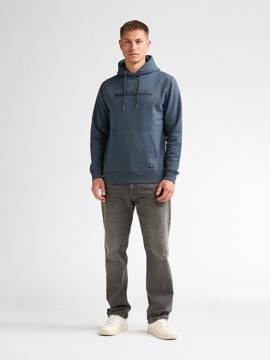 Man draagt een blauwe hoodie met Petrol Industries-logo, grijze jeans en witte sneakers.