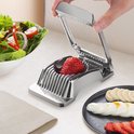 Zilveren eiersnijder snijdt een rode aardbei in plakjes. Naast een salade, geschilde eieren en aardbeienschijfjes.