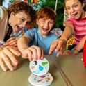 Een vrouw en twee kinderen spelen buiten Dobble met kaarten met symbolen zoals een yin-yang en een anemoon.