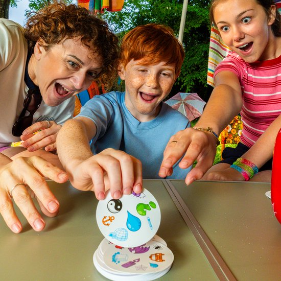 Een vrouw en twee kinderen spelen buiten Dobble met kaarten met symbolen zoals een yin-yang en een anemoon.