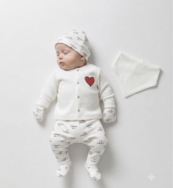 Een slapende baby draagt een witte outfit met hartjesprint, inclusief muts, trui, broek en wanten. De trui heeft een rode hartapplicatie.