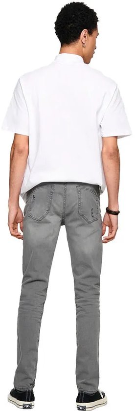 Achterkant van een man in grijze skinny jeans met scheuren en een wit T-shirt.