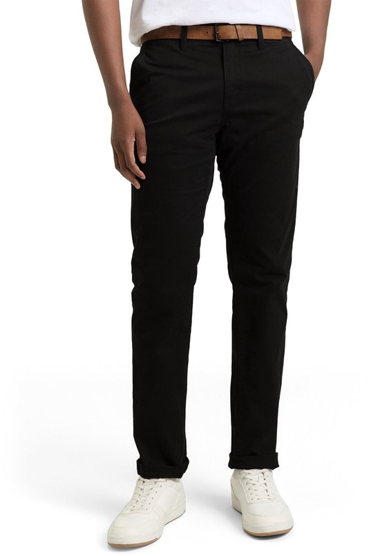 Man in zwarte chino met opgerolde broekspijpen en witte sneakers, met bruine riem.