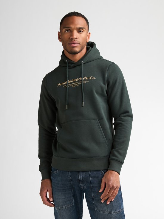 Donkergroene hoodie met ronde hals, lange mouwen, kangoeroezak en gouden tekstprint op de borst, gedragen door een man.