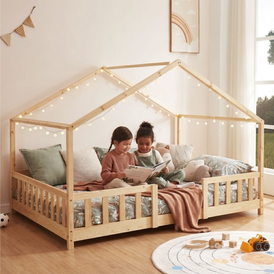 Deux enfants lisant un livre dans un lit maison en bois naturel avec barreaux et guirlande.
